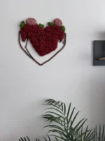 Designový prvek Ekomoss: červené mechové srdce v dřevěných rukou na stěně nad pokojovou rostlinou.
